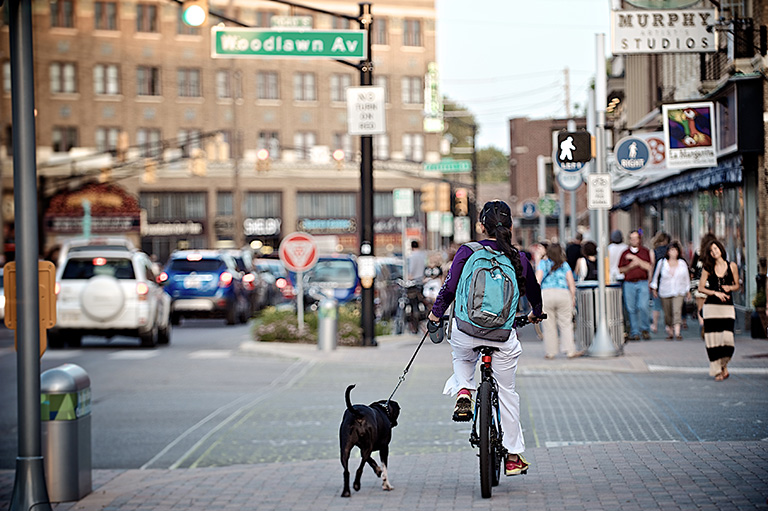 Woman riding bike through city with dog on leash