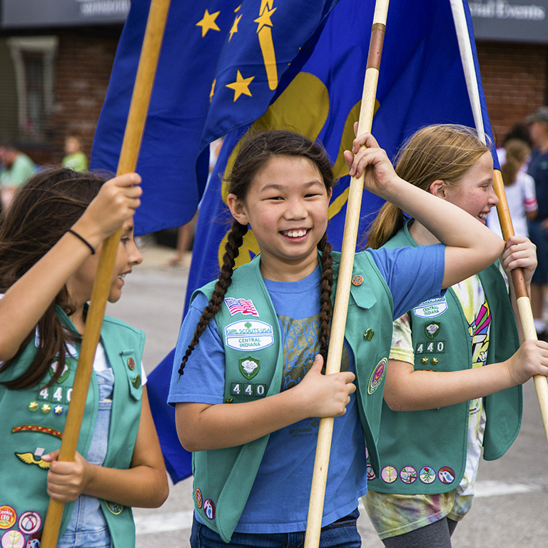 Three Girl Scouts carry flags marching in the Freedom Festival Parade