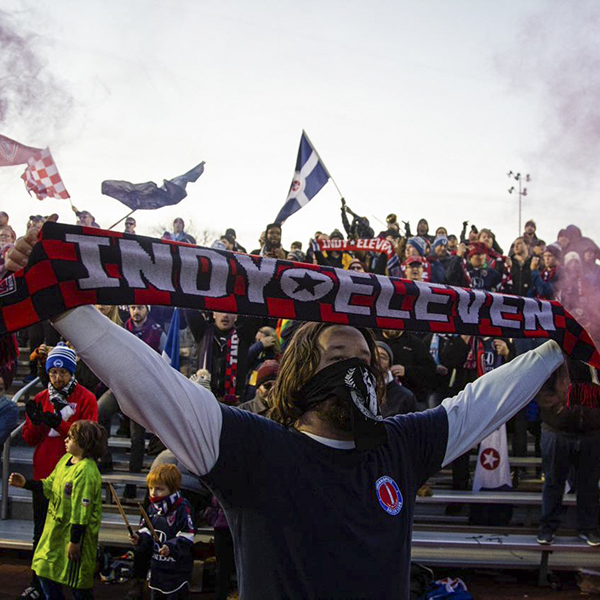 A fan holds an Indy Eleven banner over his head in front of other spectators.