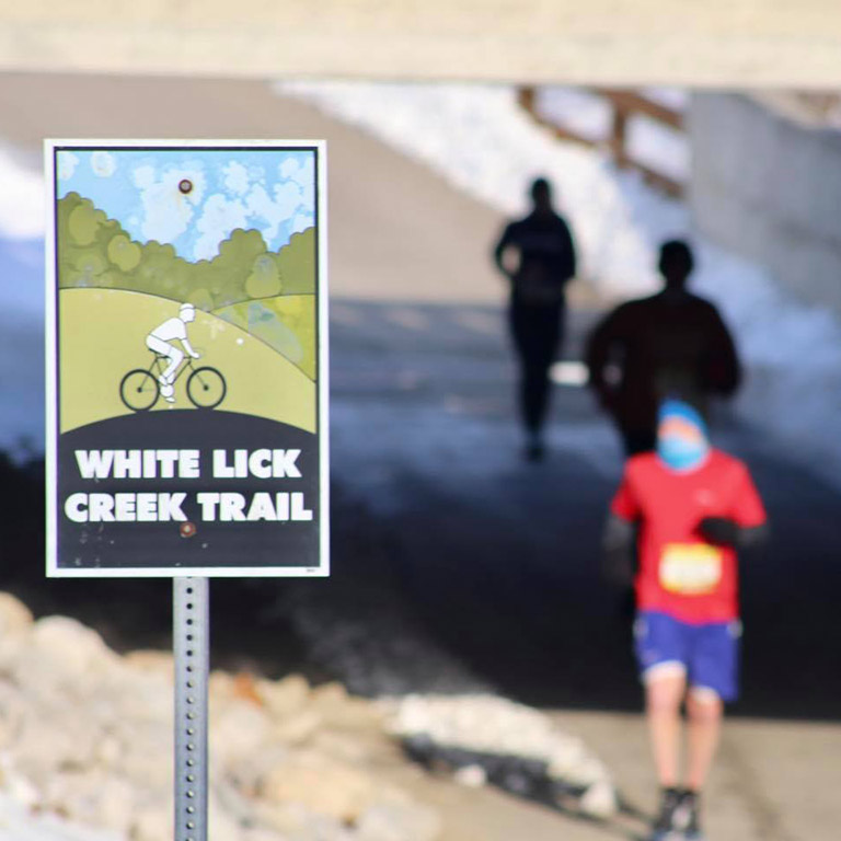 White Lick Creek Trail sign with runners out of focus in the background