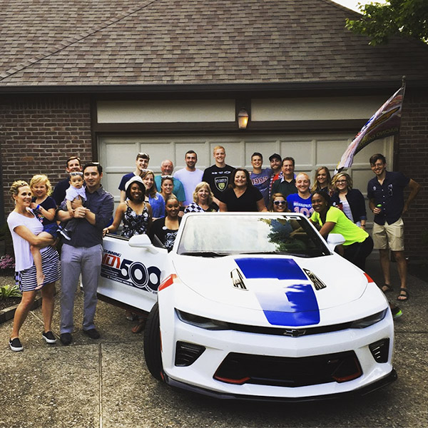 Families gather around an Indy 500 pace car at a porch party