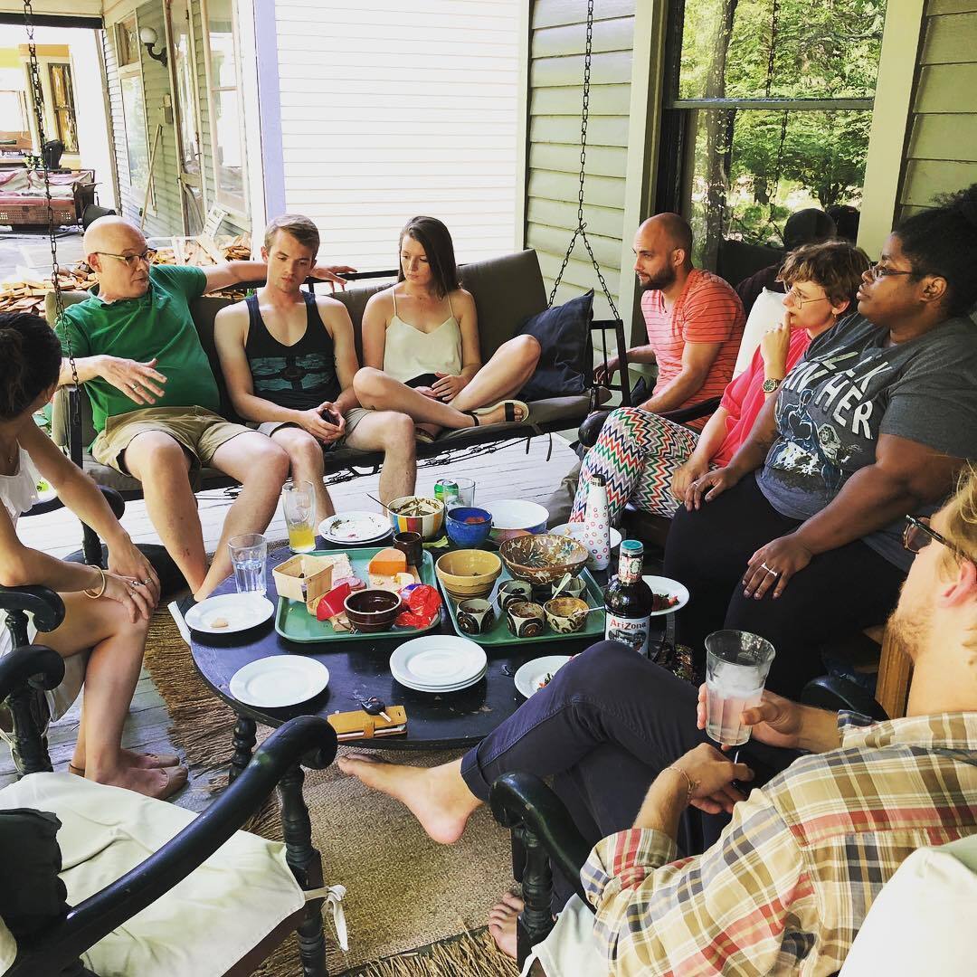 A group of people sits around the table talking at a porch party