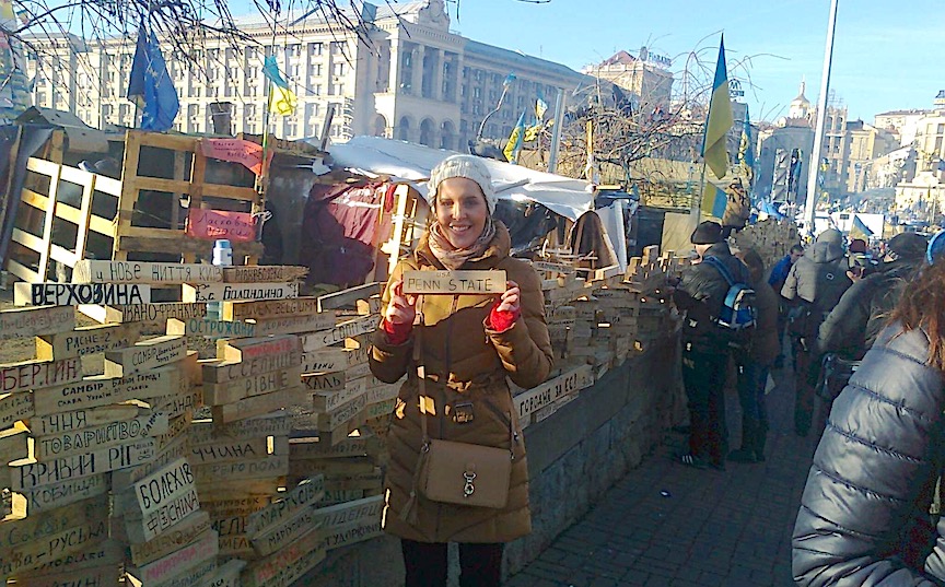 A woman stands before a wall honoring Ukraine