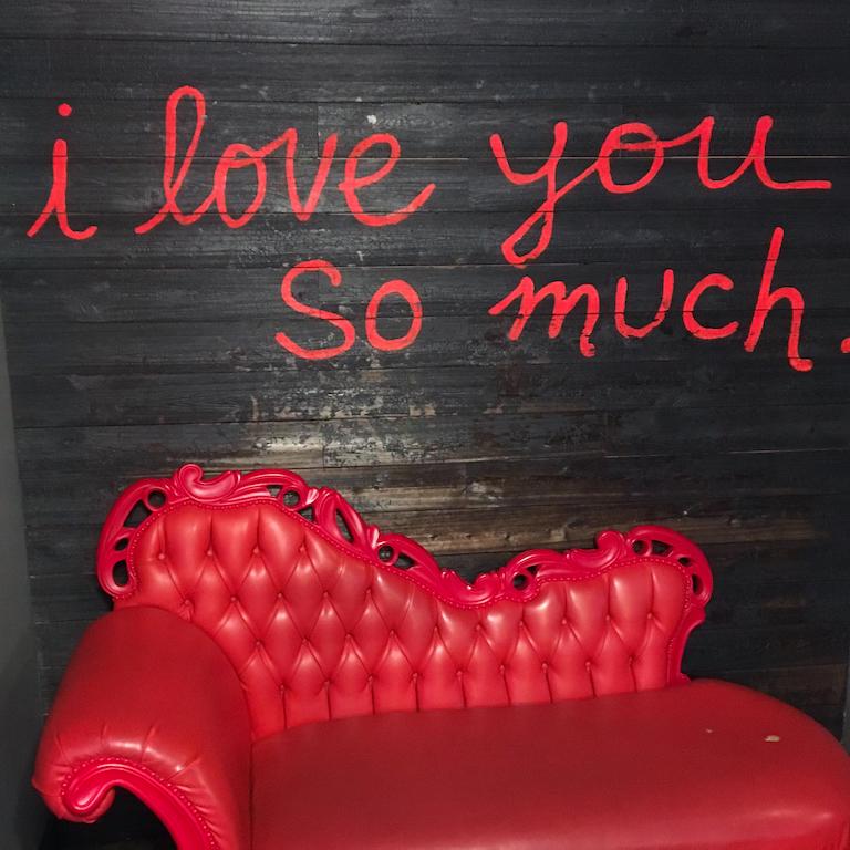Red loveseat with a neon sign that reads "I love you so much"