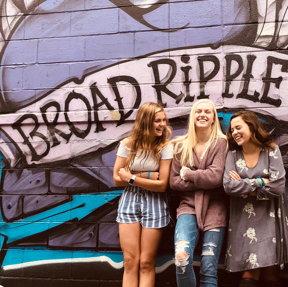 Three young woman posing in front of the Broad Ripple mural