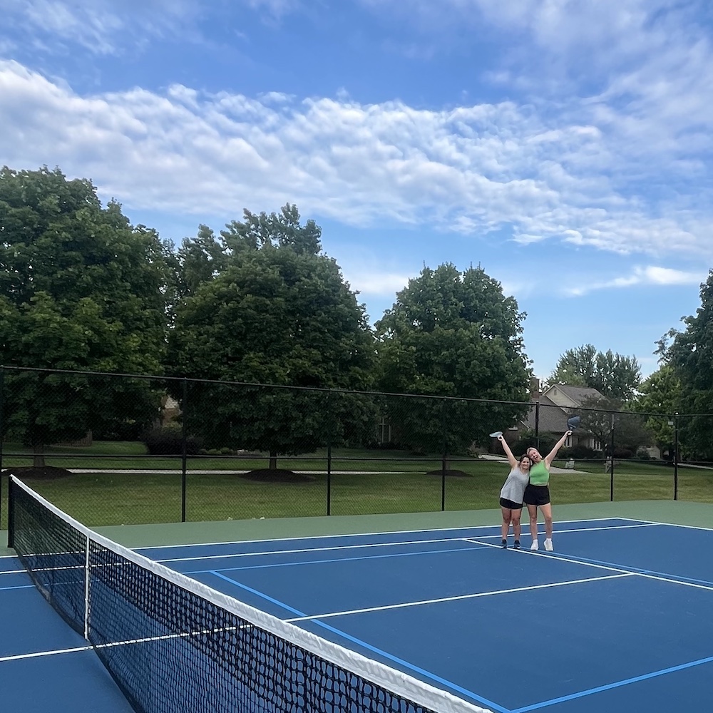 Two young woman posing on a pickleball court